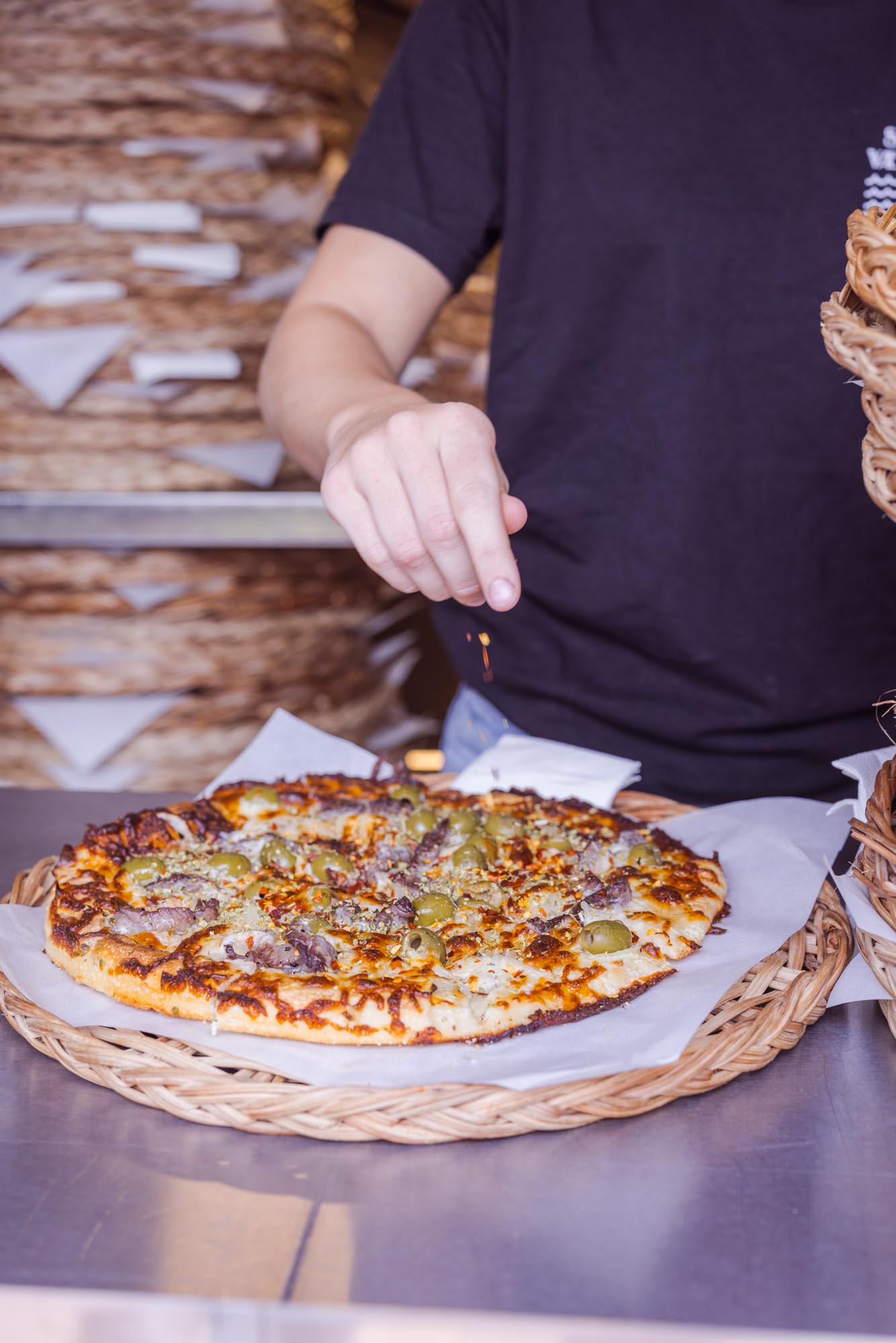 Amerikanske deep-pan pizza tilberedes på Sørens Værtshus i Snogebæk på Bornholm. En ansat strør chiliflager og oregano på den friskbagte pizza som netop er komet ud af stenovnen.