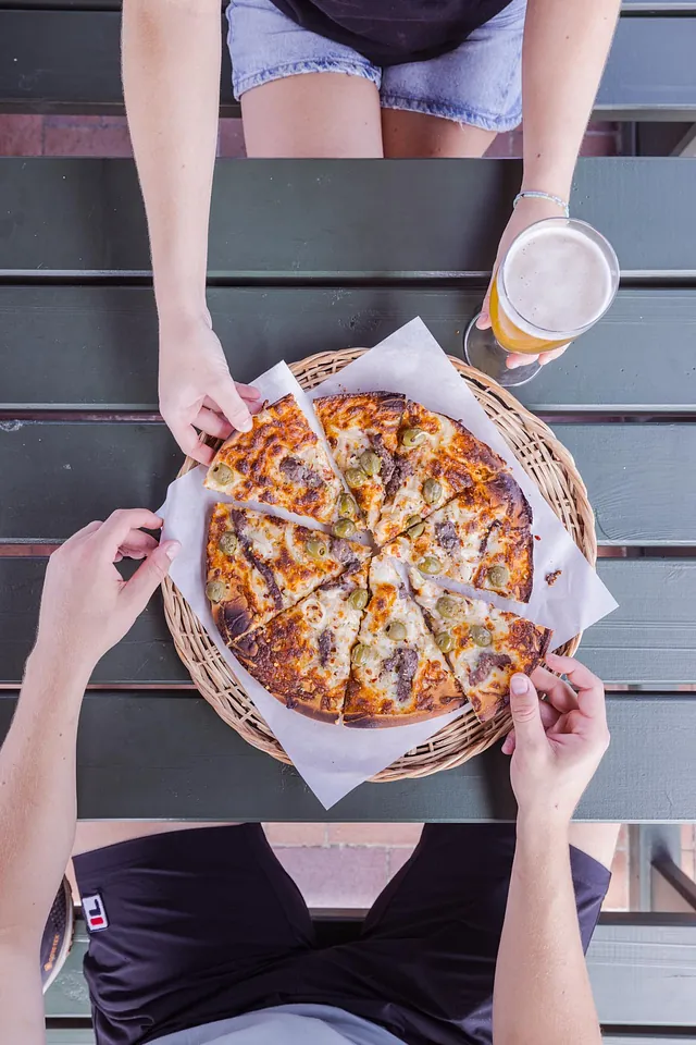 Pappas Pizza serveret på Sørens Værtshus i Snogebæk på Bornholm. Pizza set ovenfra, med hænder som tager et stykke pizza.