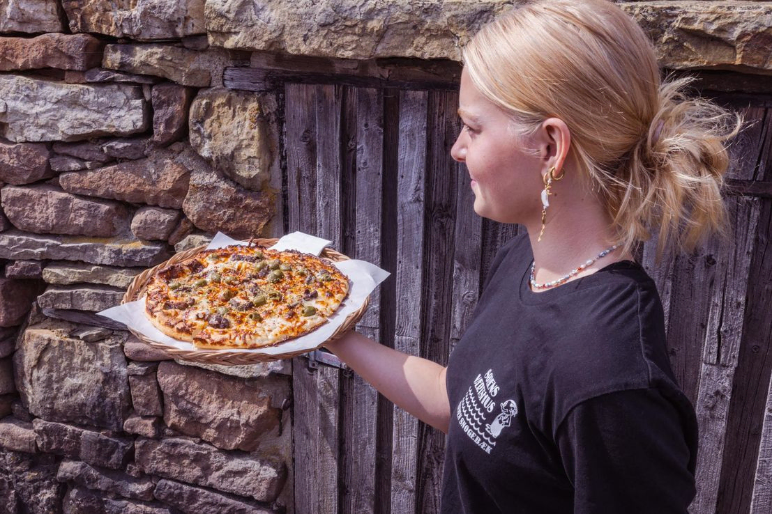 Pappas Pizza fra Sørens Værtshus i Snogebæk som skal serveres. Ung pige ses bære på pizza, som hun er på vej for at servere.