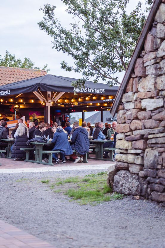 Sørens Værtshus i Snogebæk på Bornholm. Gæster får servering og man ser de idylliske omgivelser.